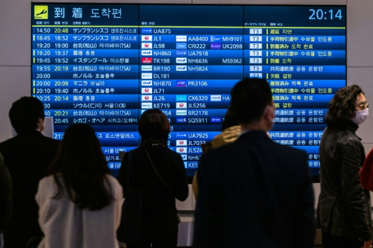 People wait in front a board showing international flight arrivals at Tokyo's Haneda international airport