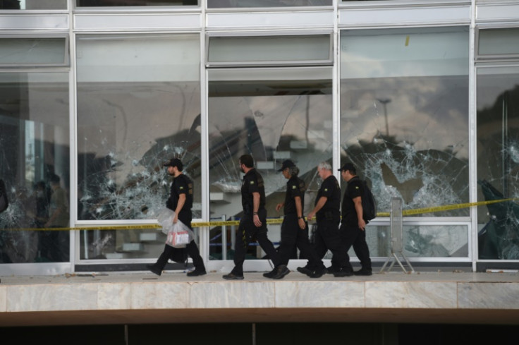 Police officers walk past vandalized windows at the Supreme Court building in Brasilia