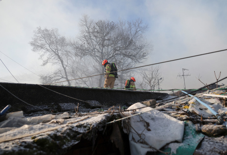 Firefighters walk on the roof of a shed at the site of a fire at Guryong village, in Seoul