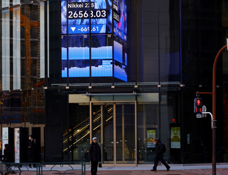 People walk past an electric board showing Nikkei index at a business district in Tokyo