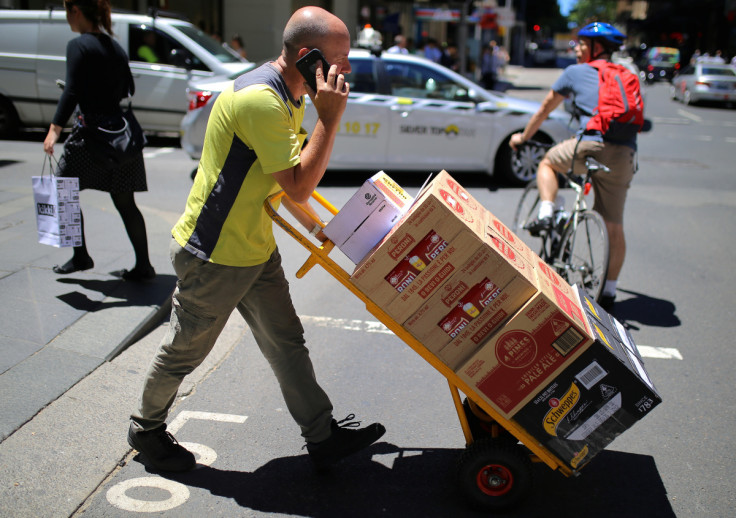 A worker talks on his phone as he pushes a trolley loaded with goods across a main road in a retail shopping area in central Sydney