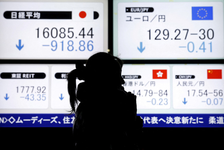 A pedestrian holding her mobile phone walks past electronic boards showing Japan's Nikkei average