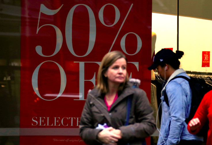 Shoppers walk in front of a retail shop displaying a sale sign in central Wellington, New Zealand