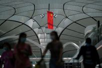 People wearing face masks walk under a Chinese flag at Beijing Daxing International Airport in Beijing
