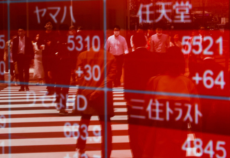 Passersby are reflected on an electric stock quotation board outside a brokerage in Tokyo