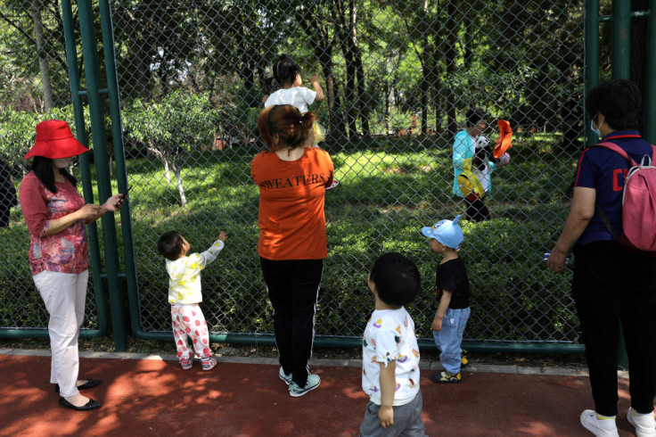 Children play next to adults at a park in Beijing