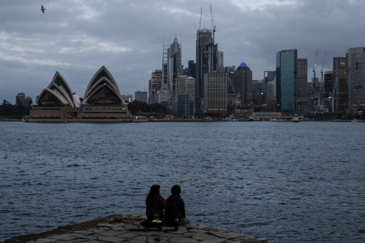 People sit on a ledge looking toward the city centre skyline and Opera House in Sydney